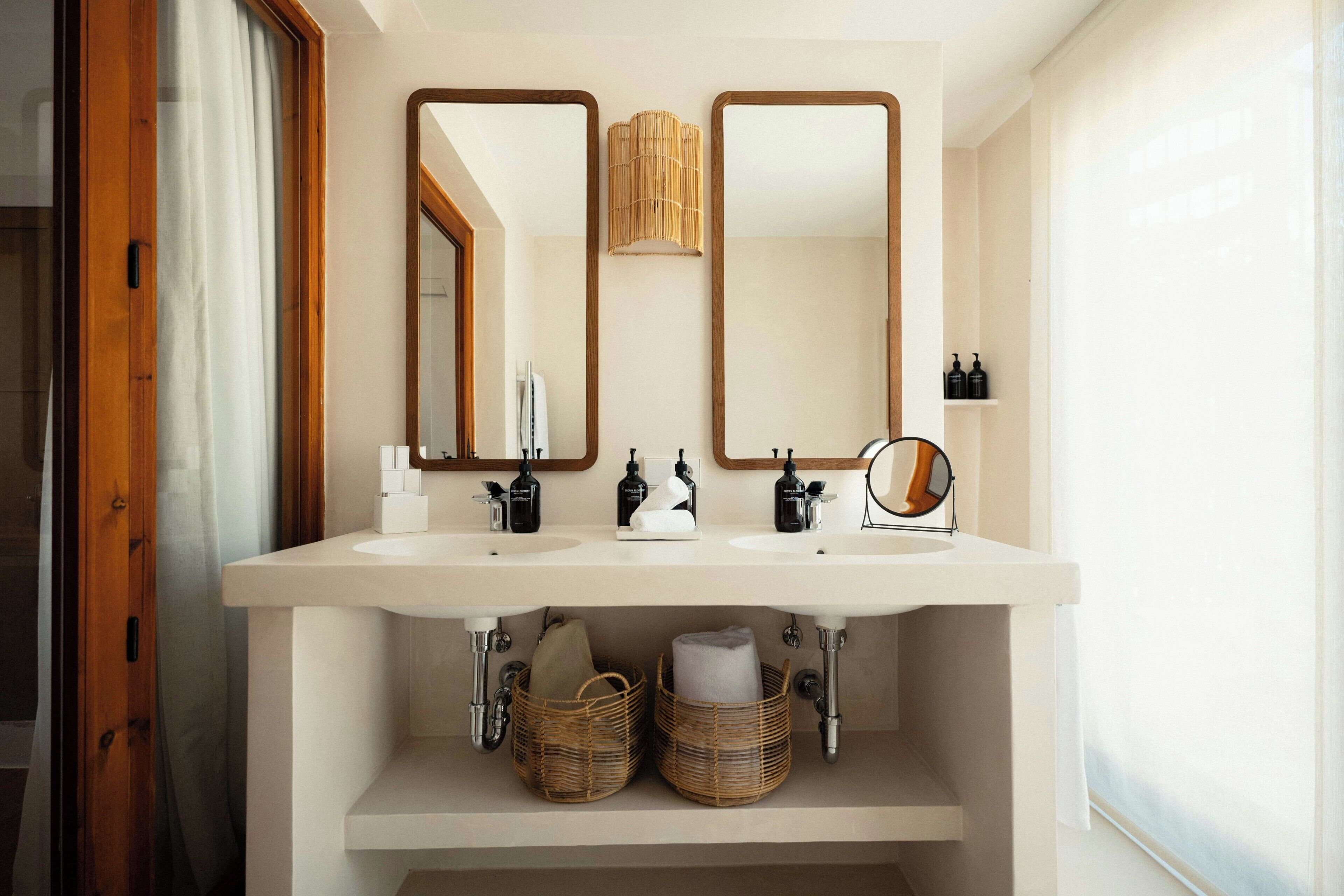 A bathroom with two sinks, mirrors, and wicker baskets under the counter.