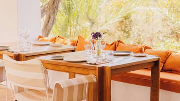 Un espace repas avec des tables et des chaises en bois, des coussins orange et des lampes suspendues.