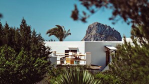 A white building with a mountain in the background, surrounded by greenery and a paved pathway. - Petunia Ibiza, a Beaumier Hotel (Sant Josep de sa Talaia)