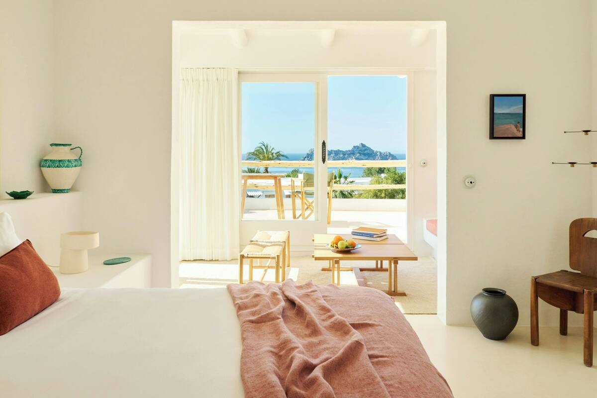 A bedroom with a bed, a table with fruit, a chair, and a view of the sea.
