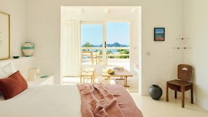 A bedroom with a bed, a table with fruit, a chair, and a view of the sea. - Petunia Ibiza, a Beaumier Hotel (Sant Josep de sa Talaia)