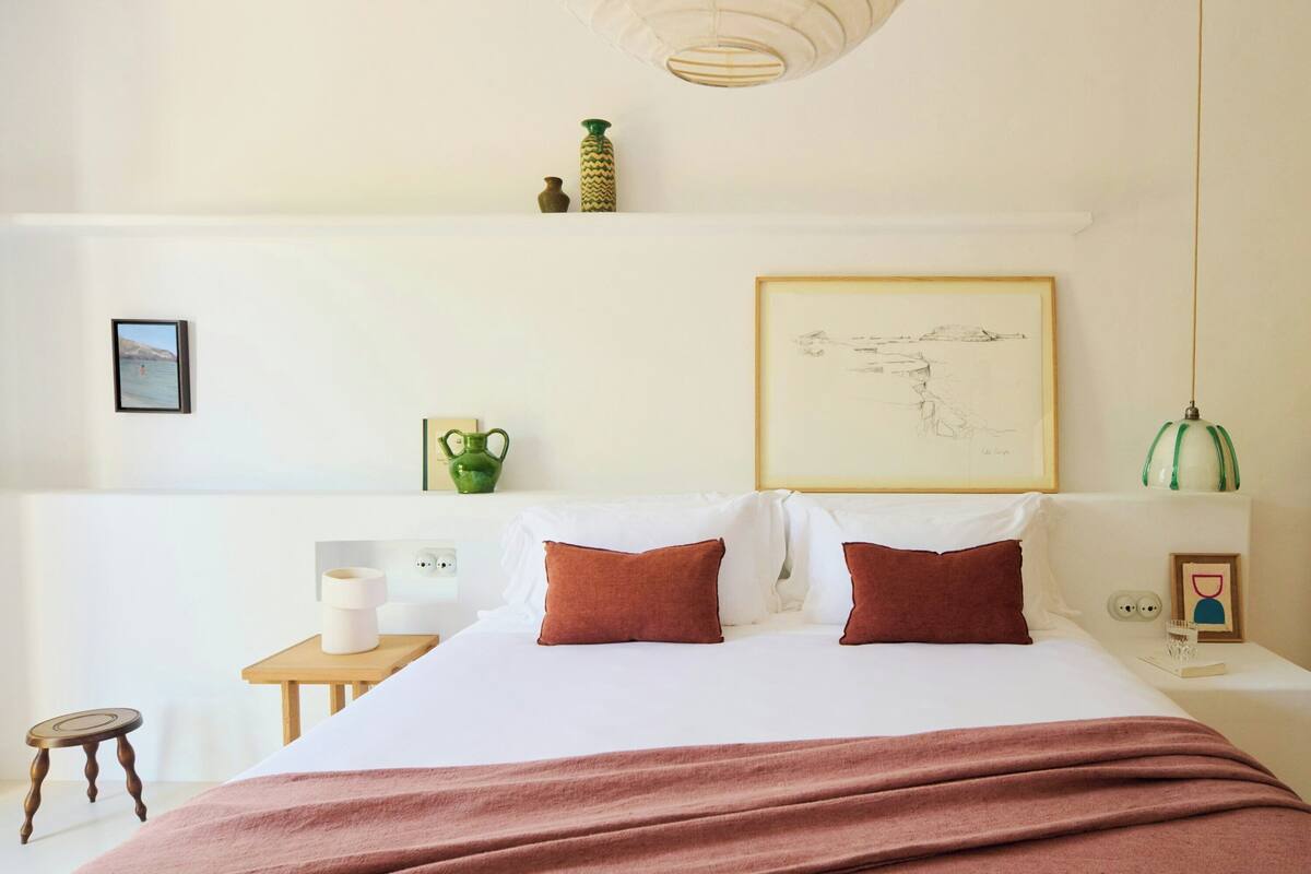 A neatly arranged bedroom with a bed, bedside tables, a mirror, and wall art.