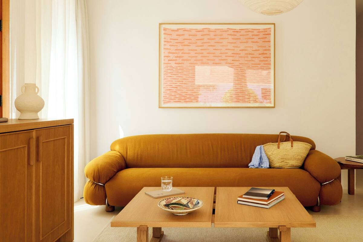 A living room with a sofa, two wooden tables, a bowl, a glass, and a book.