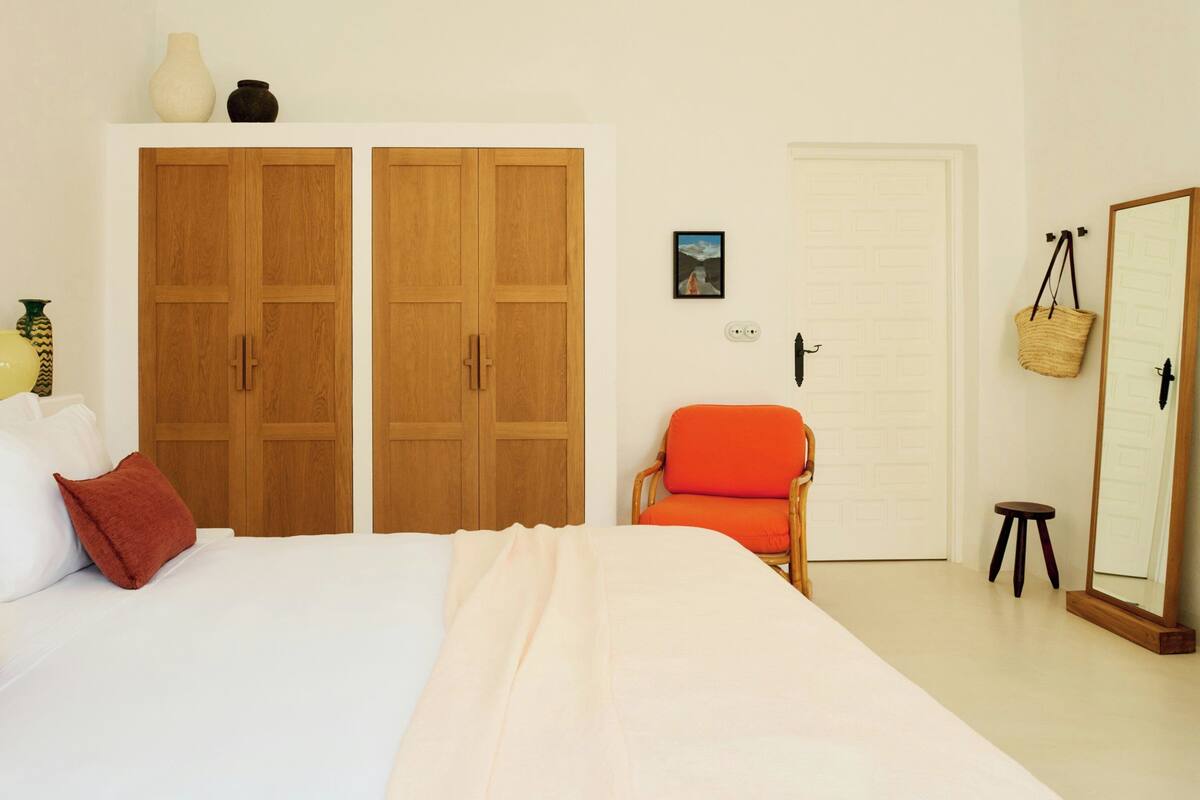 A bedroom with a bed, a wardrobe, a chair, a mirror, and a door.