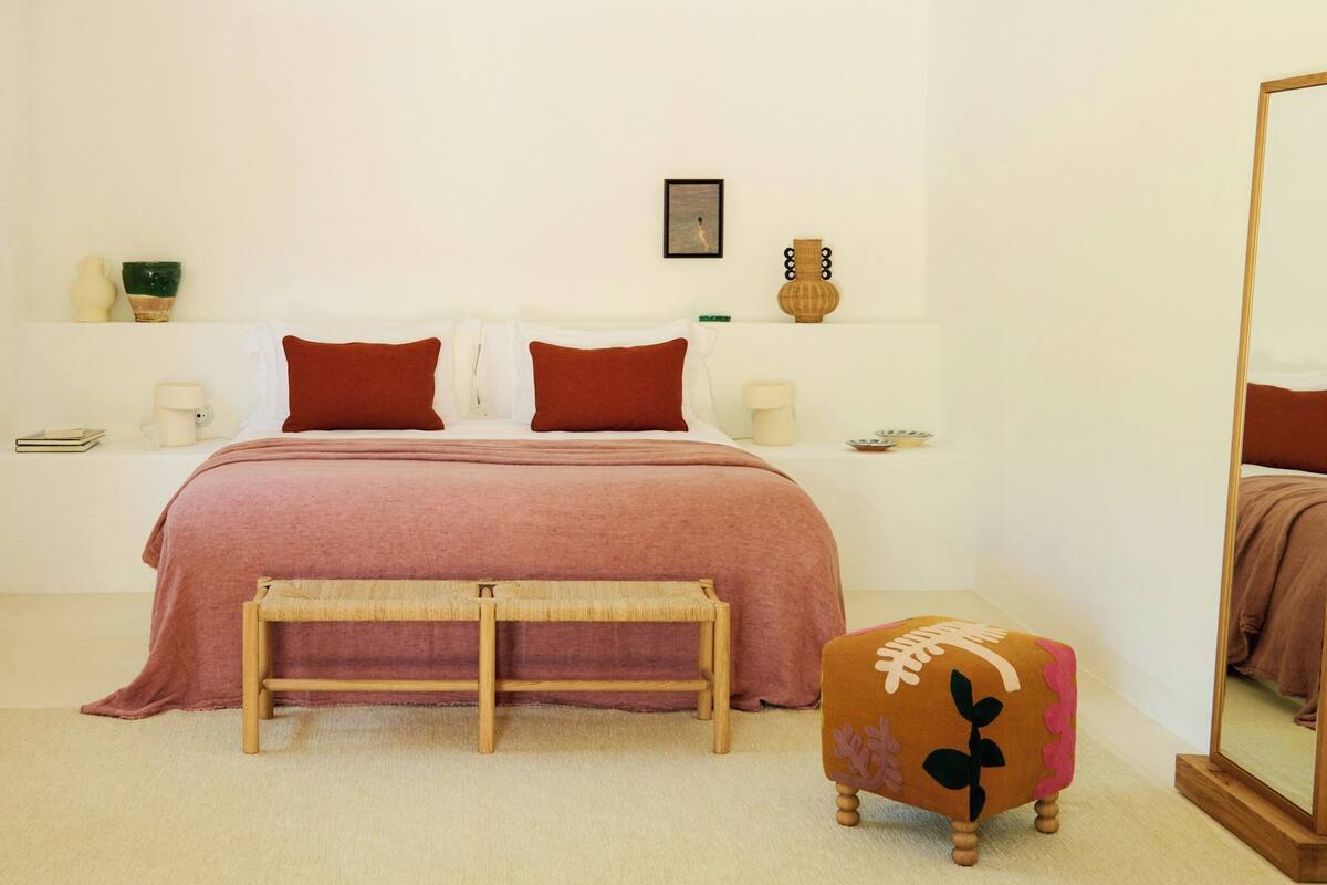 A bedroom with a bed, bedside tables, a bench, a mirror, and a small stool.