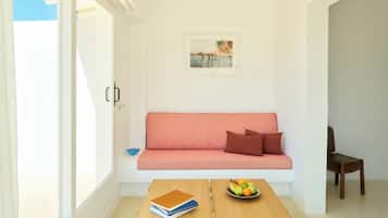 A room with a sofa, a wooden table with a bowl of fruit, and a book.