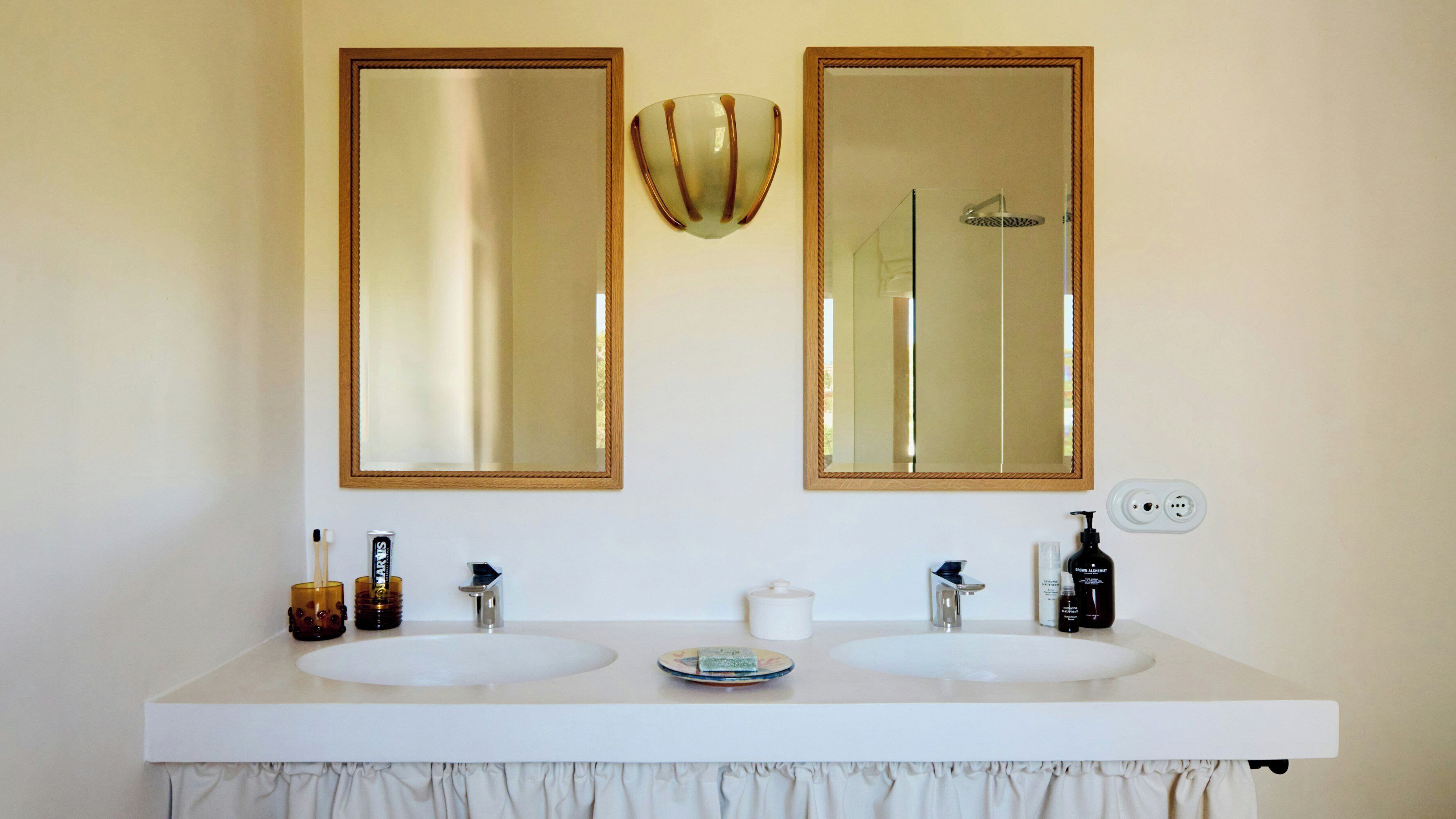 A bathroom with two sinks, a mirror, a shower, and toiletries.