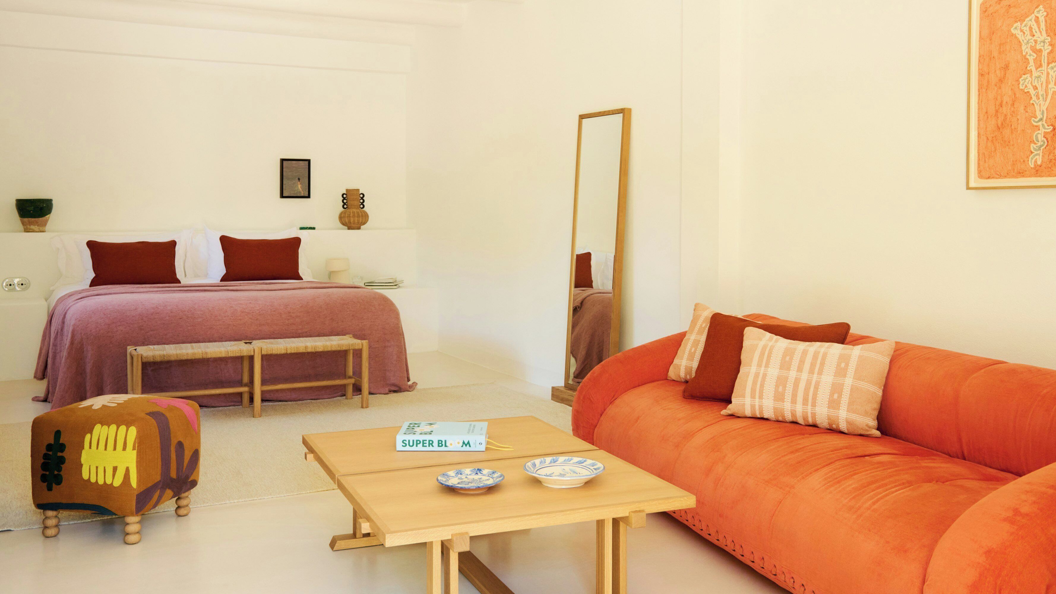 A bedroom with a bed, a sofa, a small table with bowls, and a mirror.