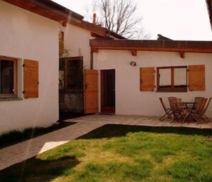 A house with a paved patio, wooden shutters, and a dining area with chairs.