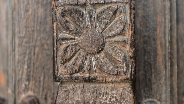 Un gros plan d’une surface en bois ornée de motifs floraux sculptés et de rivets.