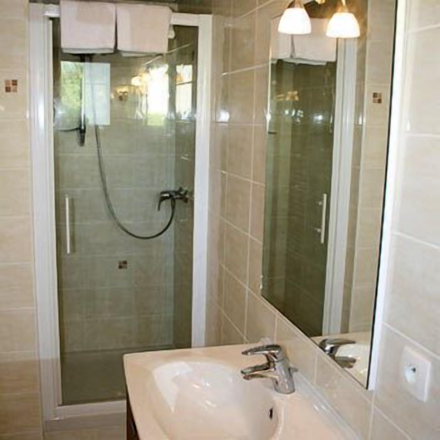 A bathroom with a glass-enclosed shower, a sink with a mirror, and tiled walls.