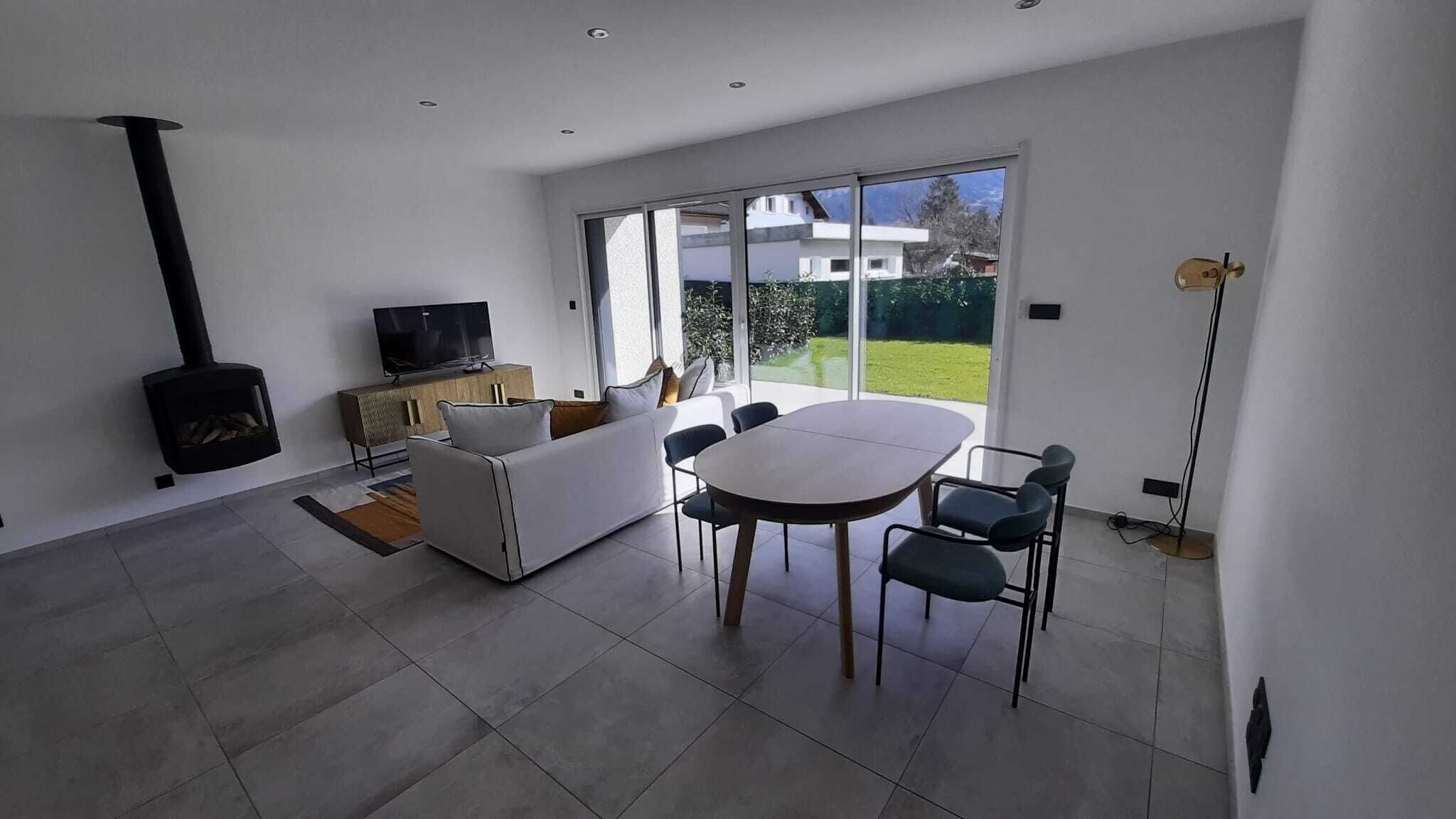 Uma sala de estar moderna com um sofá branco, uma televisão e um espaço de jantar com mesa e cadeiras.