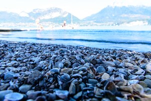 Uma praia com um primeiro plano rochoso e vista para o mar e montanhas ao fundo.