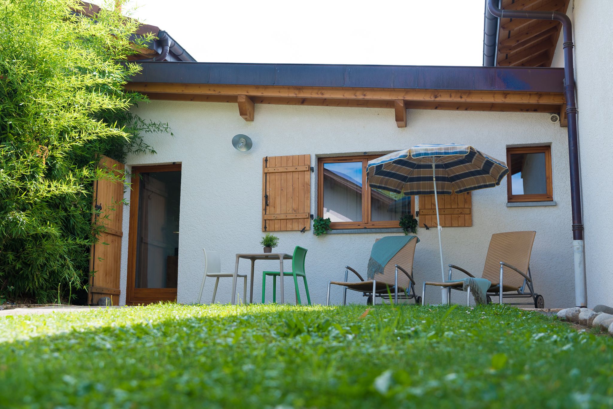 Una casa con rivestimento in legno, una finestra con persiane, un patio con tavolo e sedie e un prato verde.