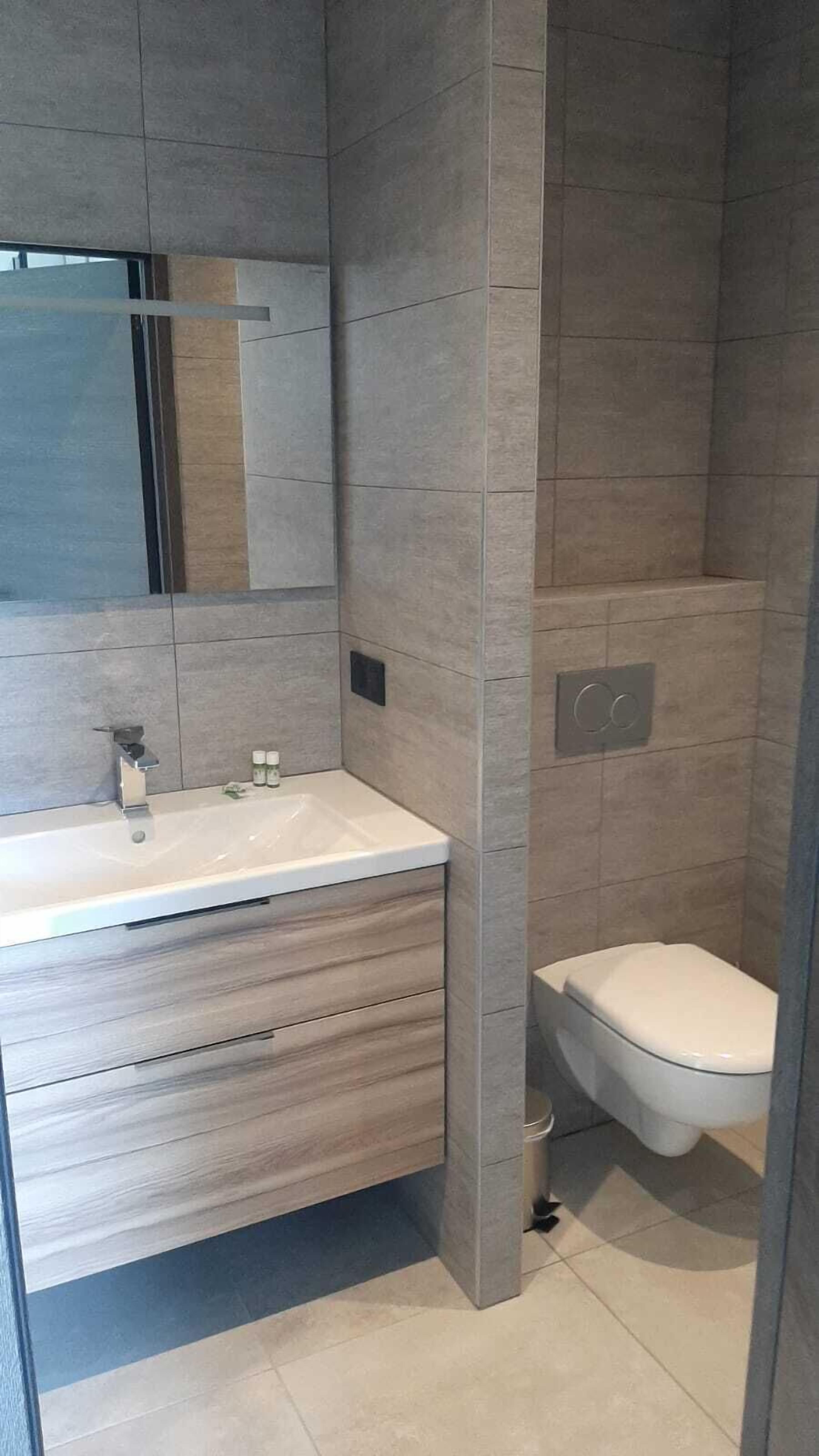 A modern bathroom with a large mirror, a sink, and a toilet.