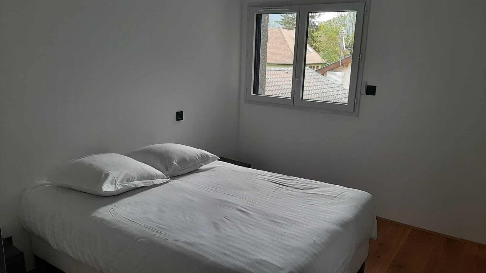 A single bed with white bedding in a room with a window.