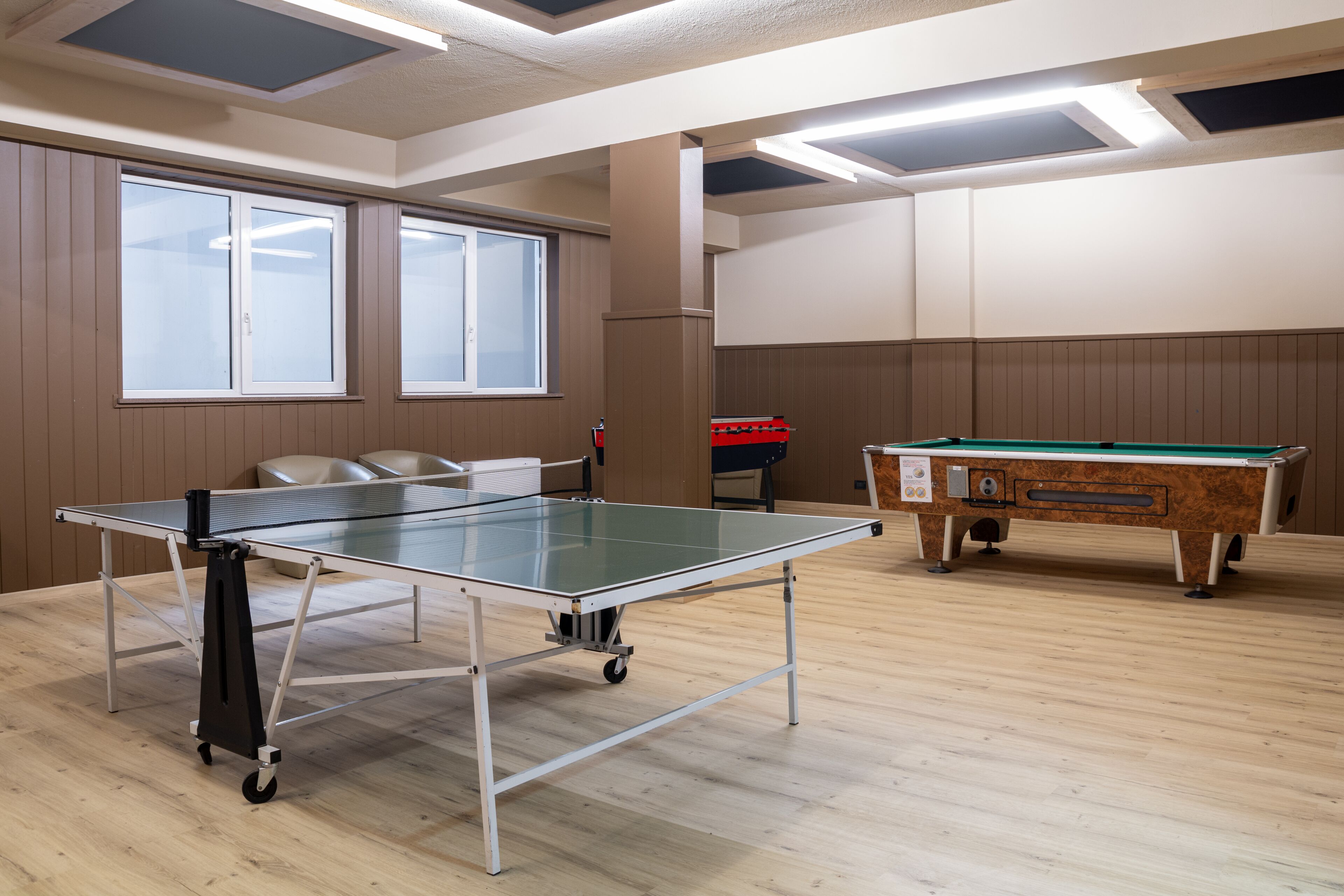 Una habitación con mesa de ping pong, mesa de billar y ventanas amplias.