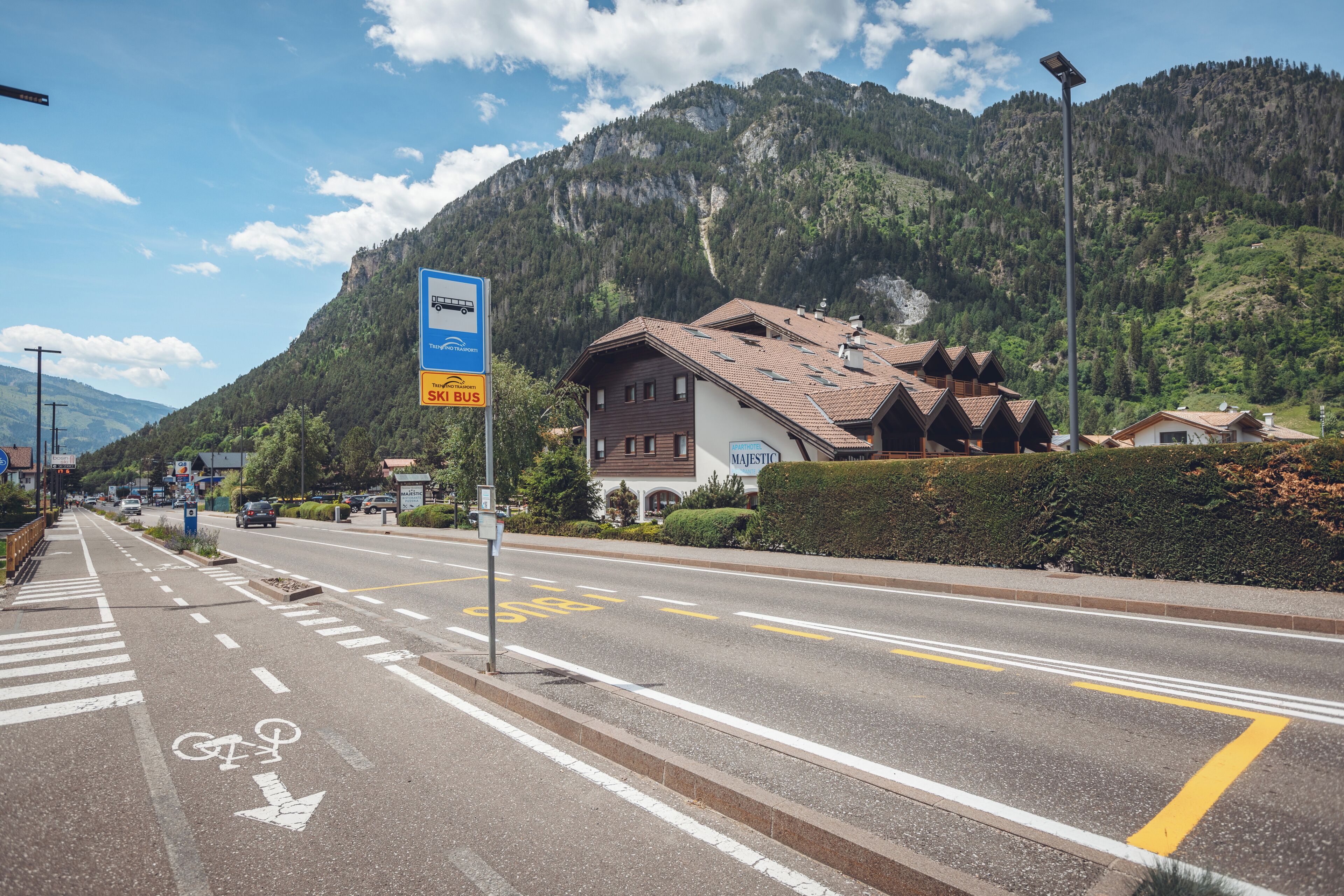 A mountain road with a bus stop sign, a building with a sloped roof, and a mountain in the background.