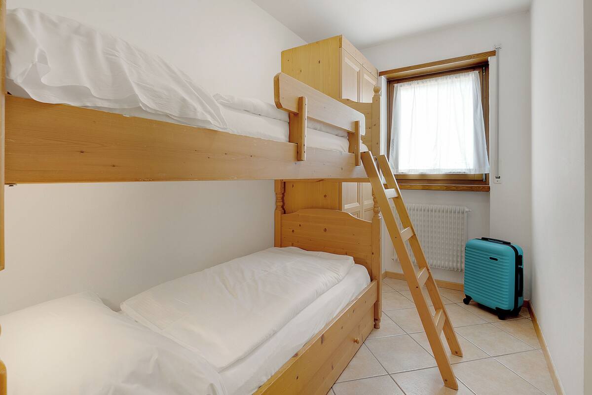 A bunk bed with a ladder, a suitcase, and a window with curtains.