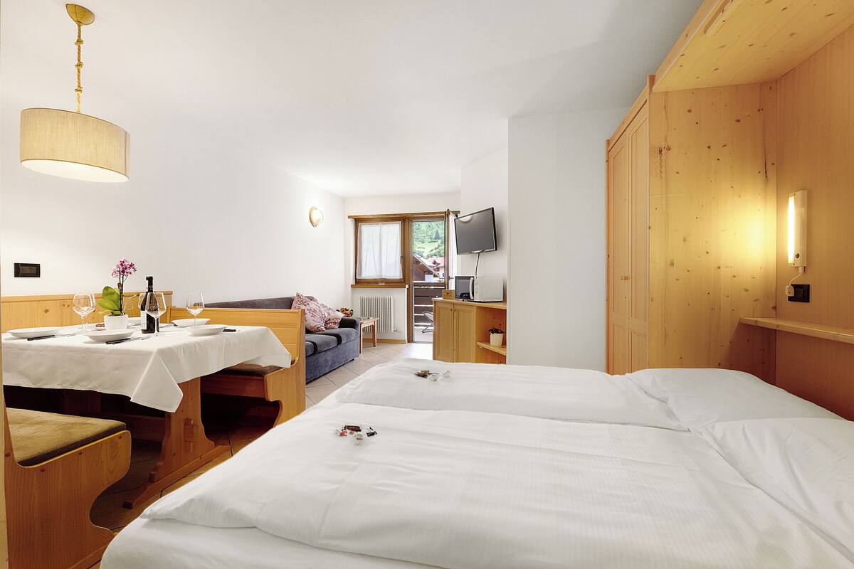 A hotel room with two beds, a dining table, a sofa, a TV, and a window with a view.