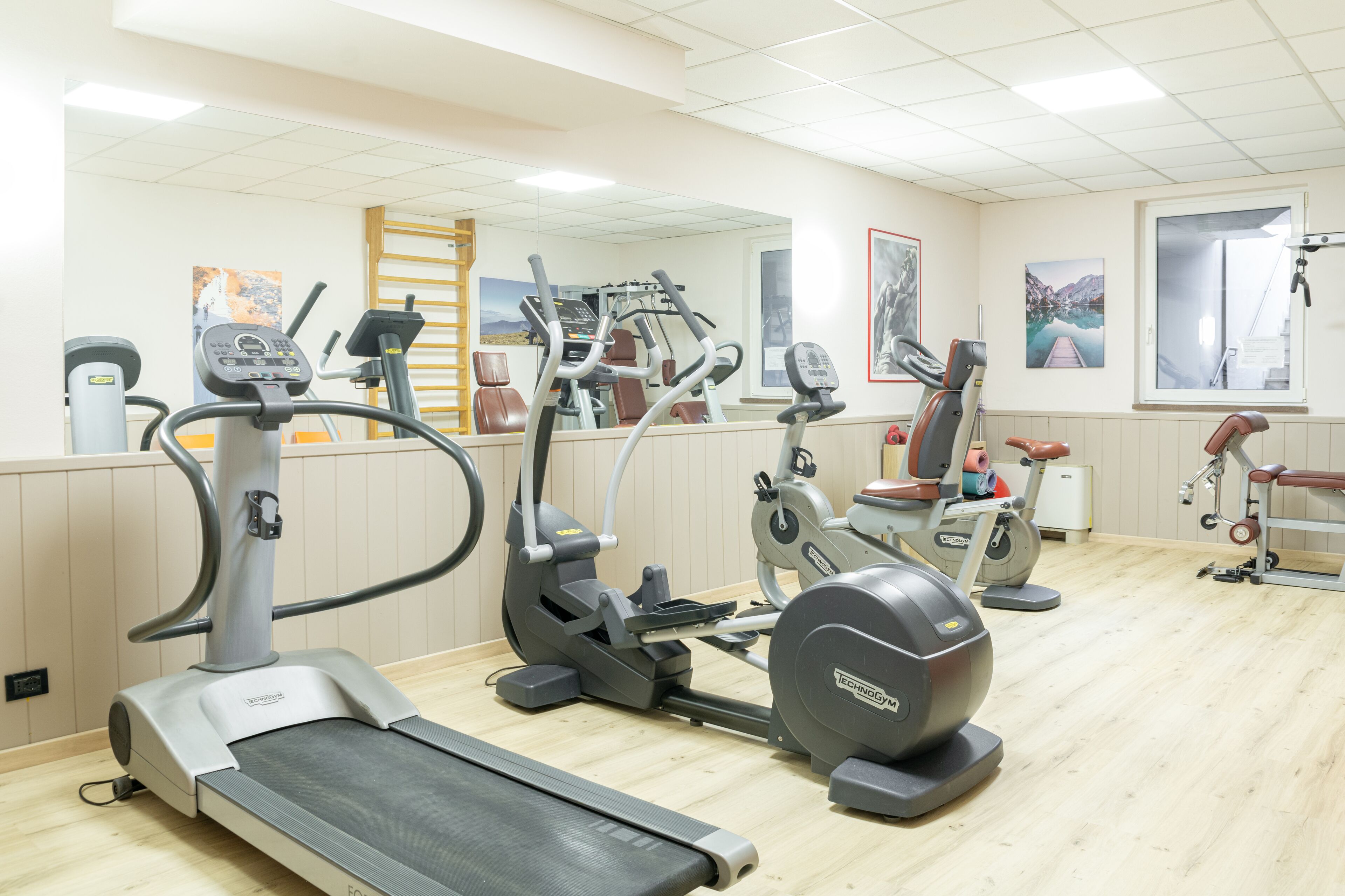 A gym with various exercise machines, a mirror, and artwork on the walls.