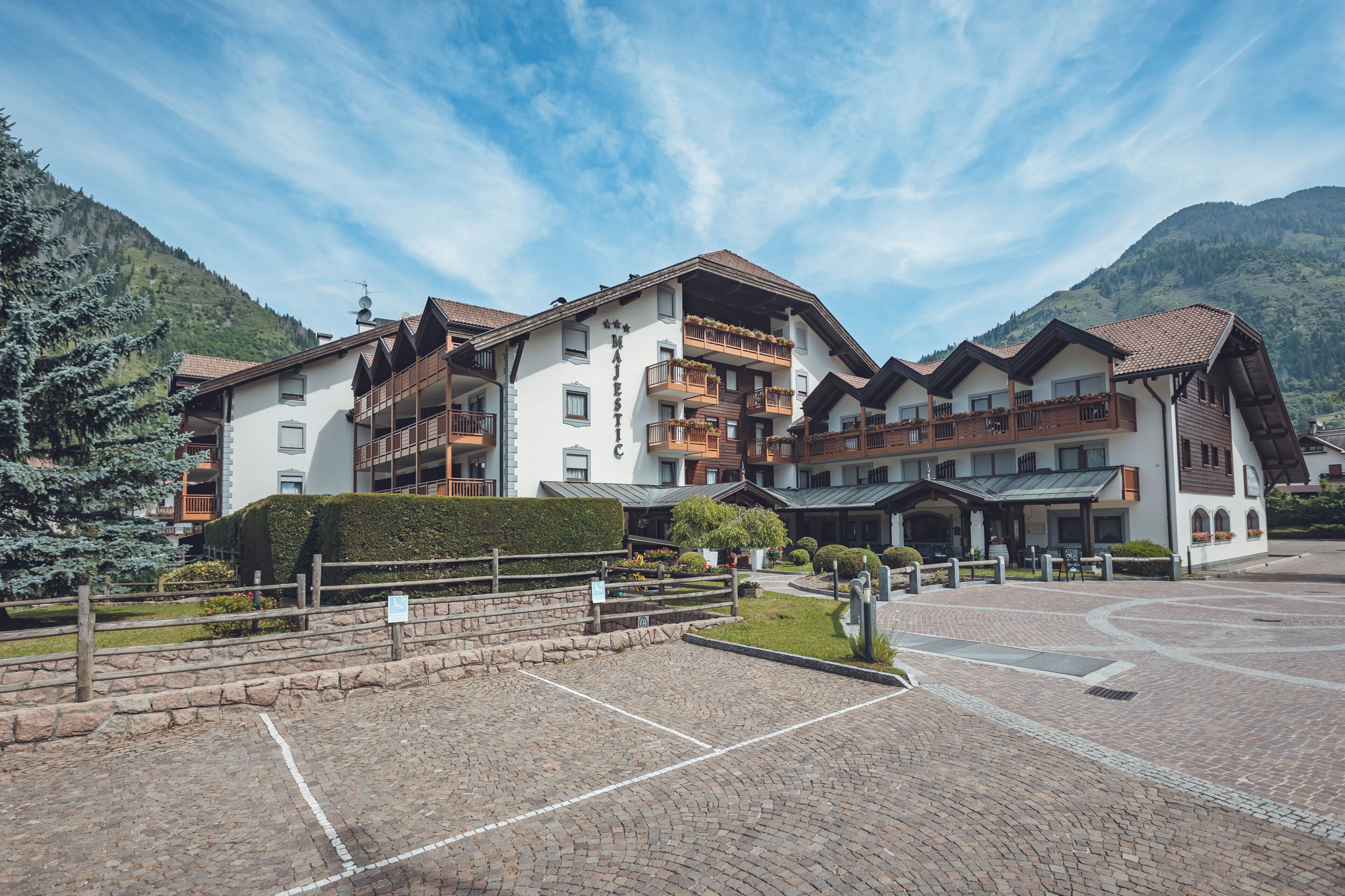 Un hotel de varios pisos con balcones, un patio interior y vistas a las montañas.