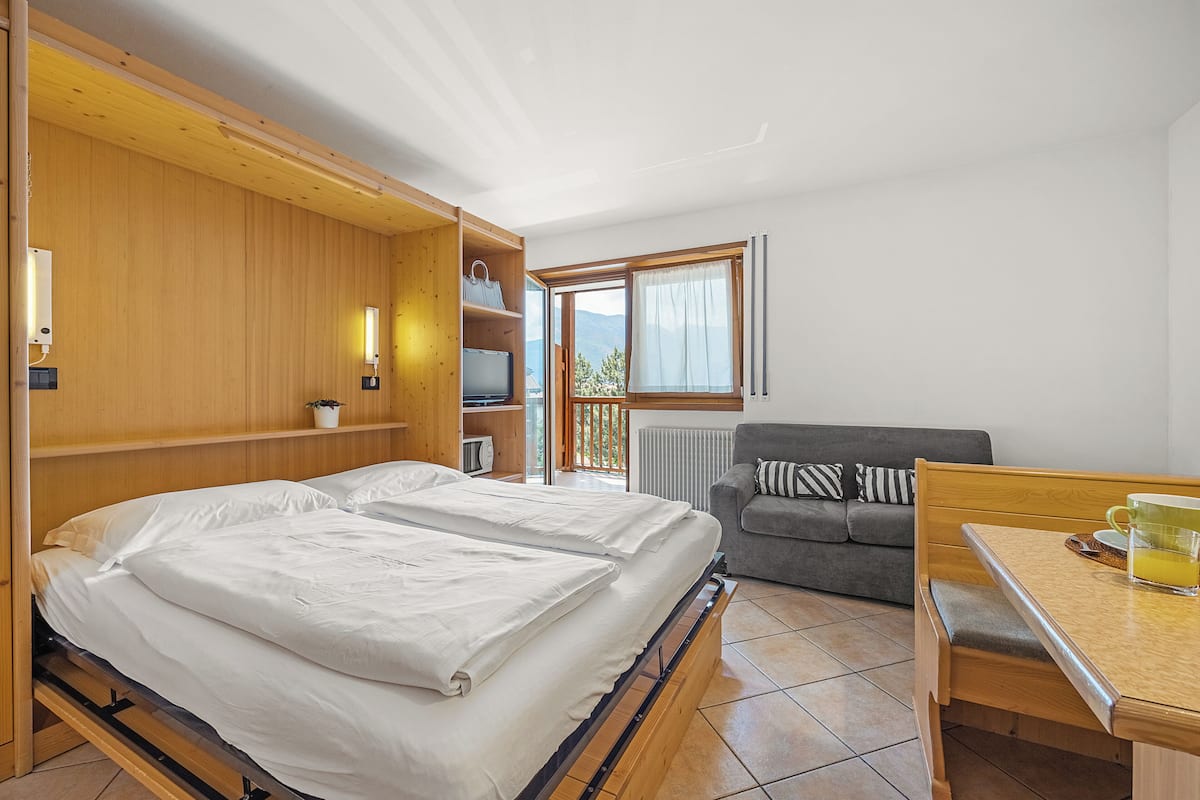 A room with a bed, a sofa, a table with a cup, and a window with a view.