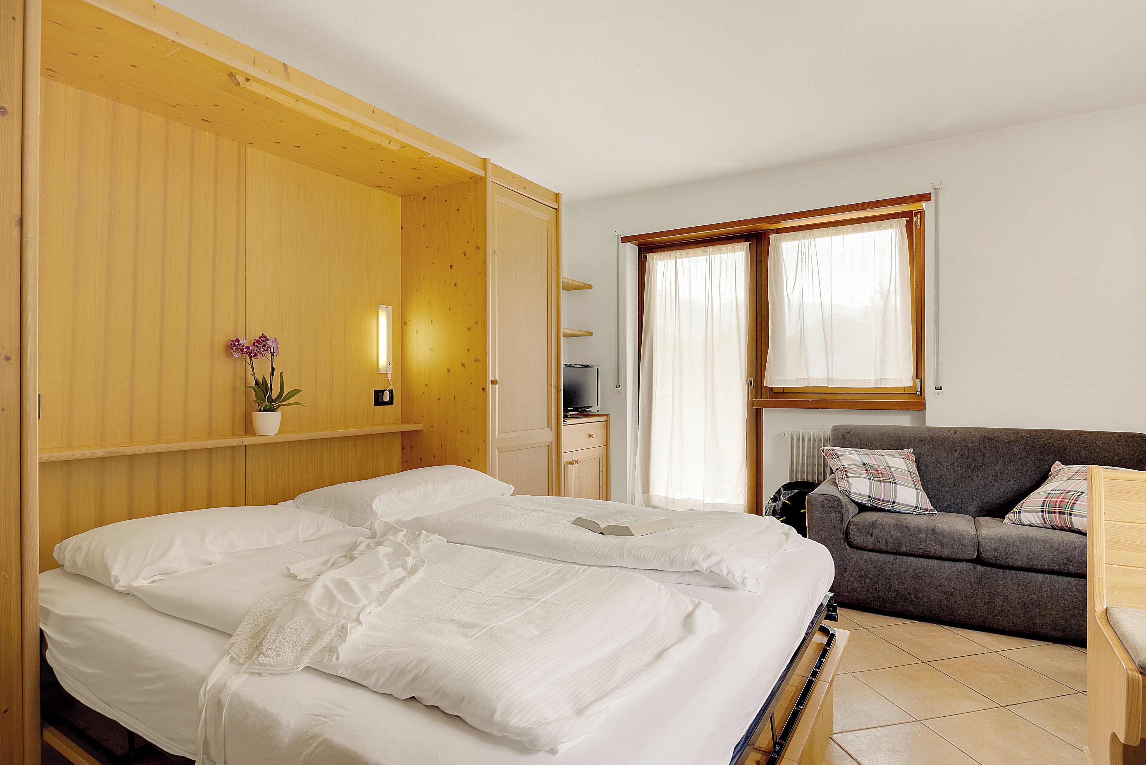 Una habitación con cama, sofá, mesita, televisor y ventana con cortinas.