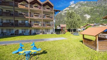 Un hotel a più piani con balconi, un'area giochi e uno sfondo montuoso.