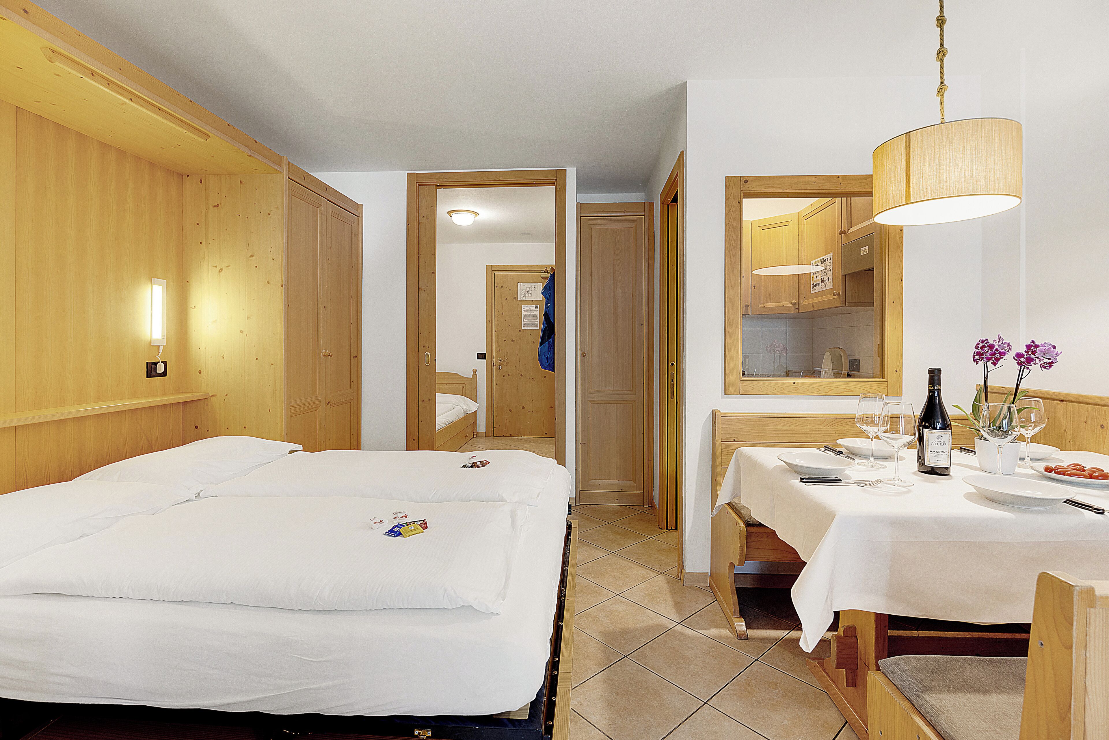A hotel room with a bed, a dining table set for two, and a mirror above the table.