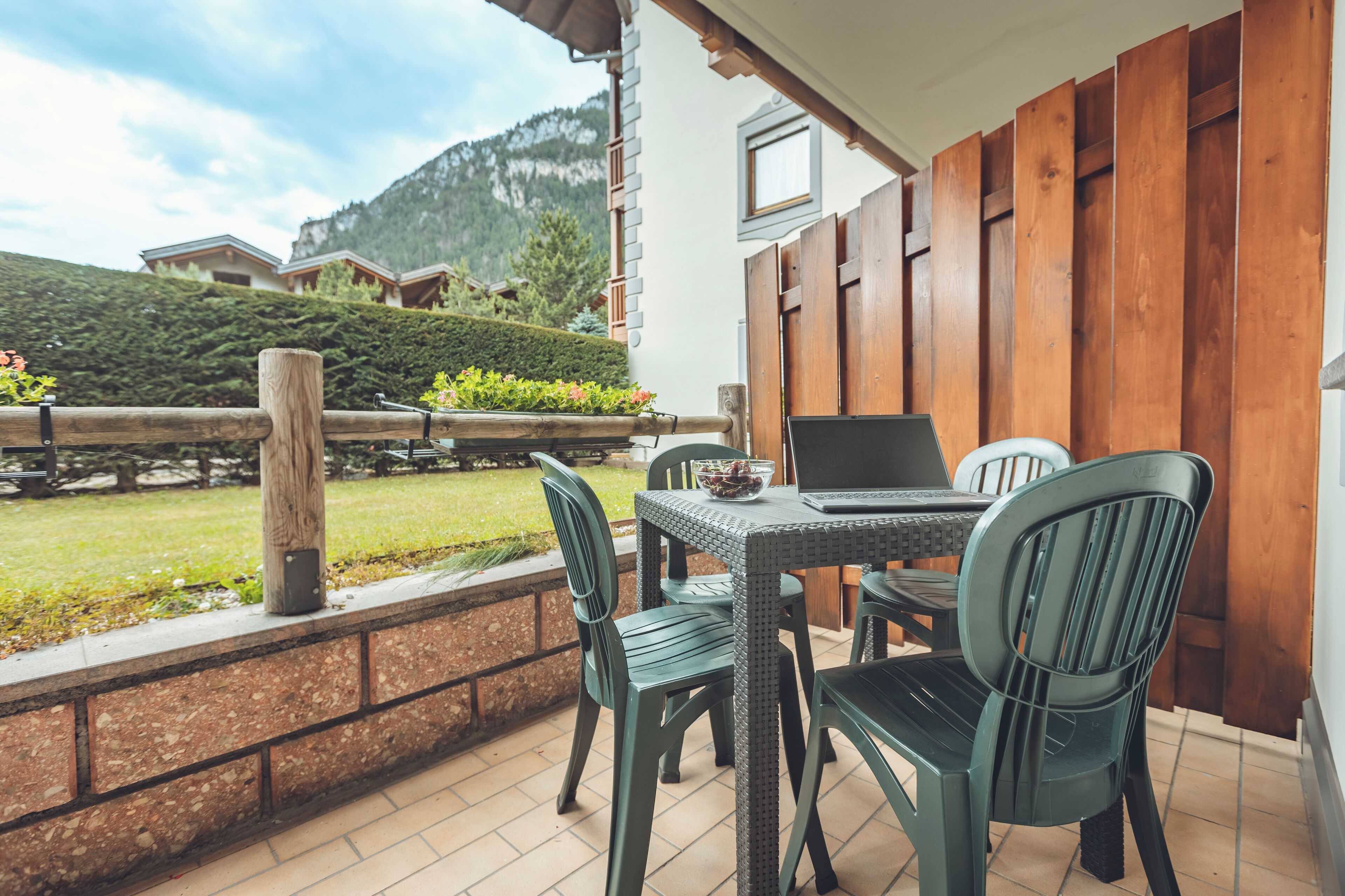 Une terrasse avec une table et des chaises, un ordinateur portable et un saladier rempli de fruits.
