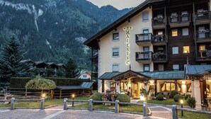 A hotel with a mountain backdrop, multiple balconies, and a well-lit entrance area. - Aparthotel Majestic (Predazzo)