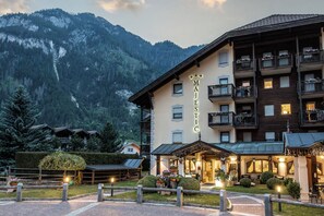 A hotel with a mountain backdrop, multiple balconies, and a well-lit entrance area. - Aparthotel Majestic (Predazzo)