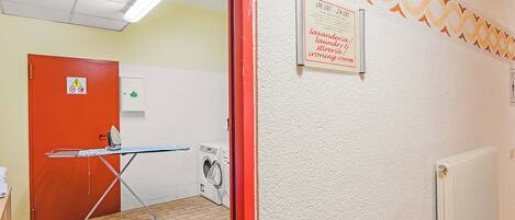 A laundry room with an ironing board, a washing machine, and a sign indicating laundry hours.