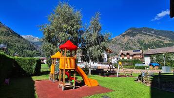 Children can play on the multi-level play structure with a slide, surrounded by lush greenery and residential buildings.