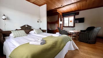 A hotel room with a large bed, two bedside tables, a chair, a small table, and a window.