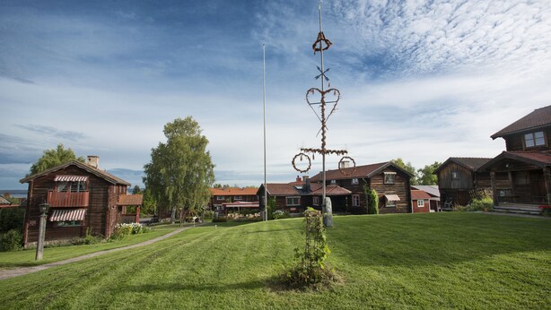 A rustic wooden house with a well-maintained lawn and a tall decorative metal structure in the center. - Klockargården Hotell (Tallberg)