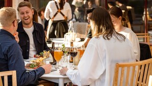 A group of people dining at an outdoor restaurant with tables set with food and drinks. - Klockargården Hotell (Tallberg)