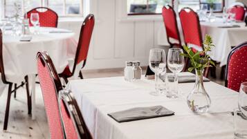 A dining area with round tables, red upholstered chairs, and white tablecloths.