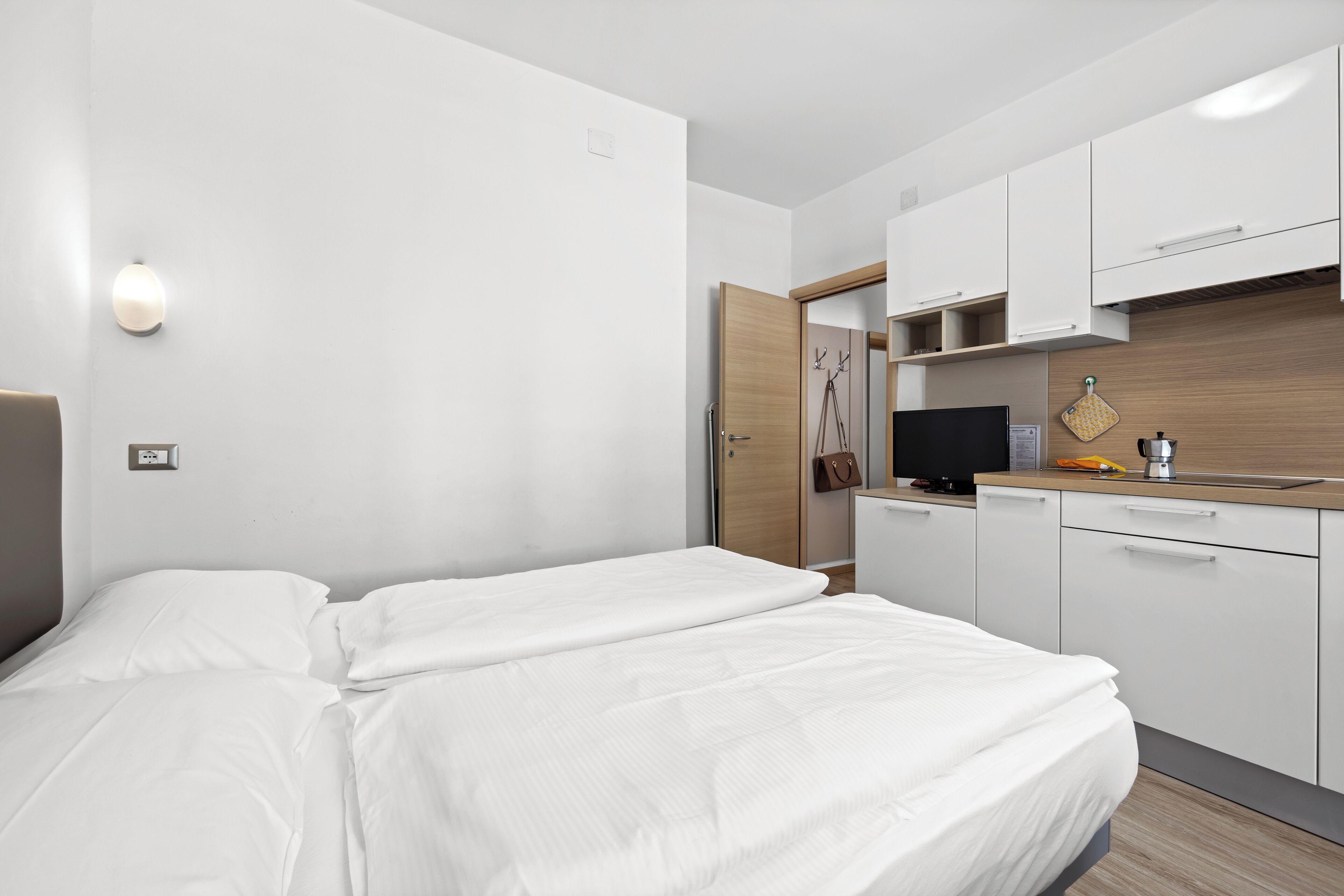 A modern hotel room with a bed, a small kitchenette, and a TV.
