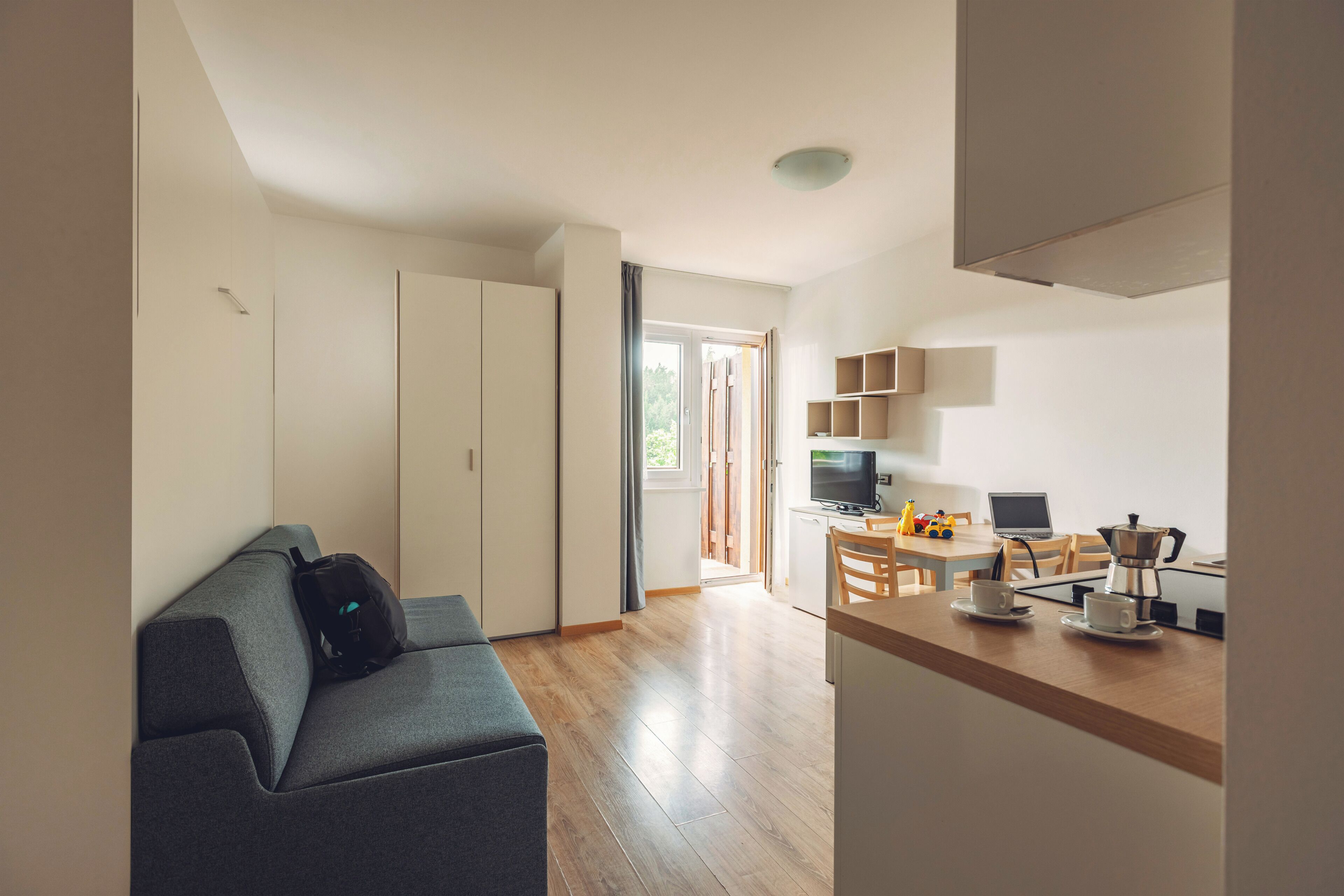 Un espace de vie moderne comprenant un canapé, un coin repas avec une table et des chaises, une kitchenette et une porte coulissante donnant sur un balcon.