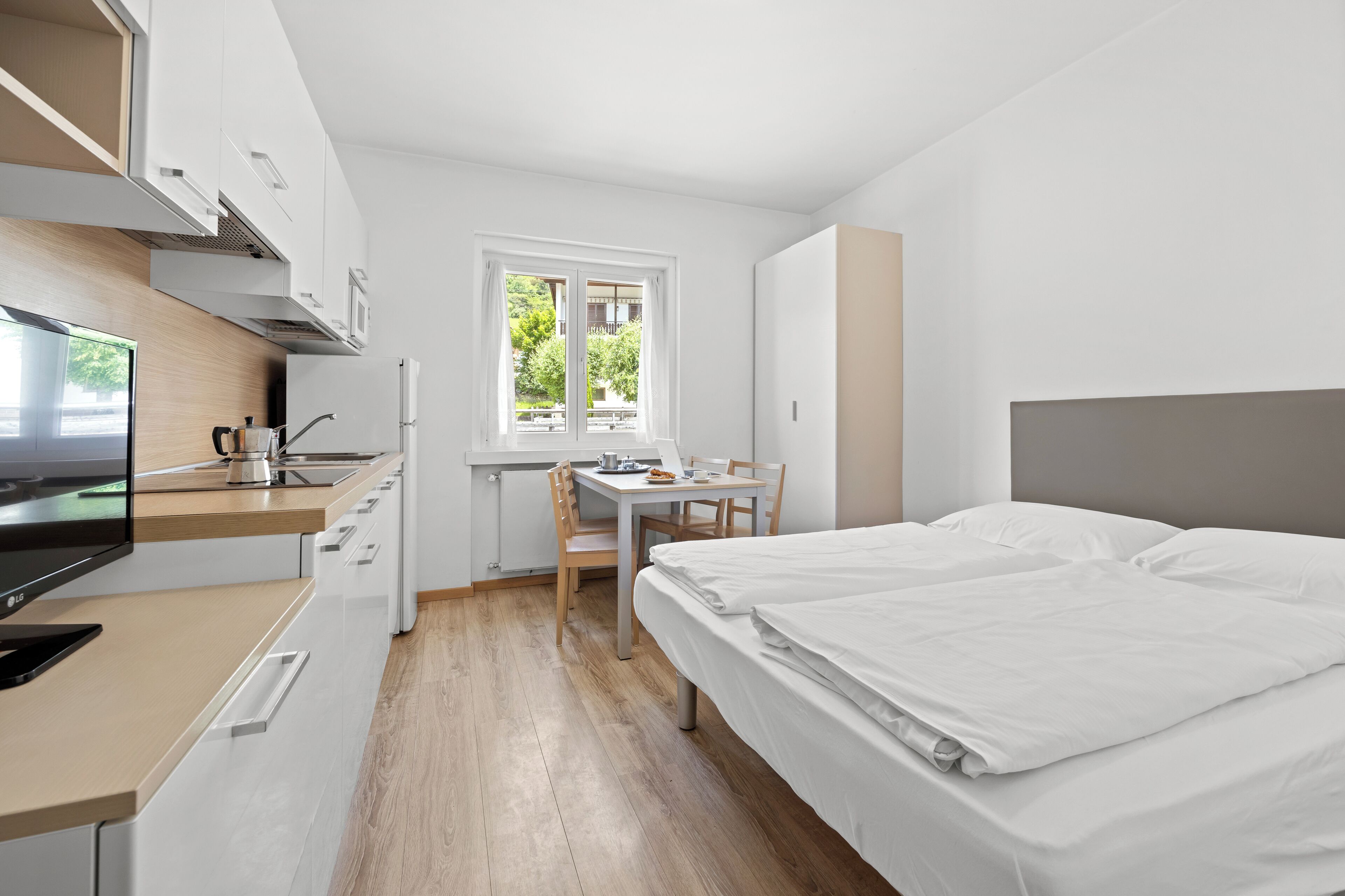A modern, compact room with a kitchenette, a dining area, and a bed.