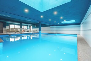 An indoor swimming pool with clear water, a sunroof, and seating areas. - Residence Lagorai (Tesero)