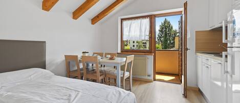 Un dormitorio con cama, una mesa de comedor con sillas, una zona de cocina y vistas al exterior.