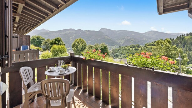 A balcony with a wooden railing, a table with chairs, and a view of mountains. - Residence Lagorai (Tesero)