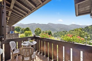 A balcony with a wooden railing, a table with chairs, and a view of mountains. - Residence Lagorai (Tesero)
