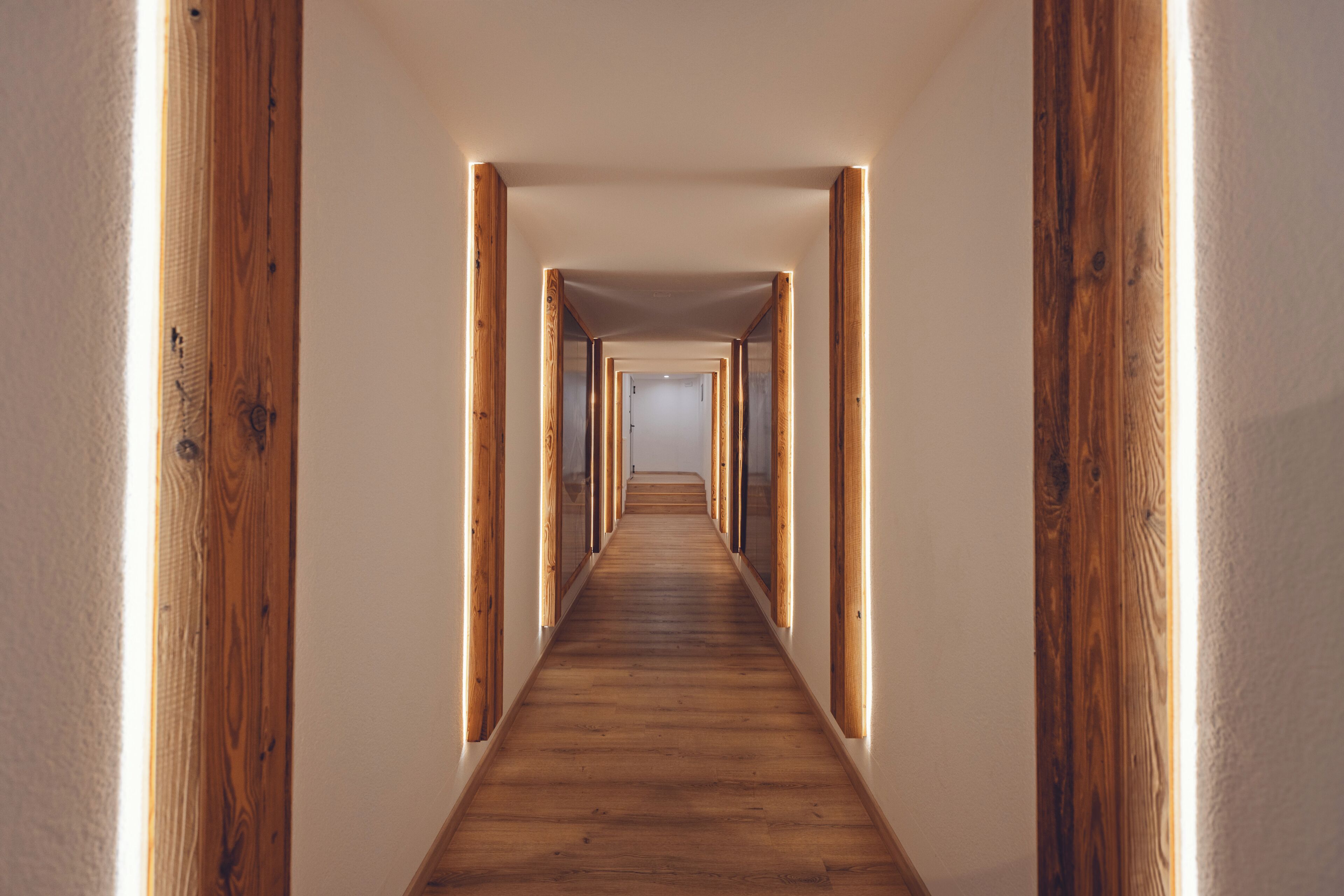 A long, narrow hallway with wooden beams and a wooden floor, leading to a door at the end.
