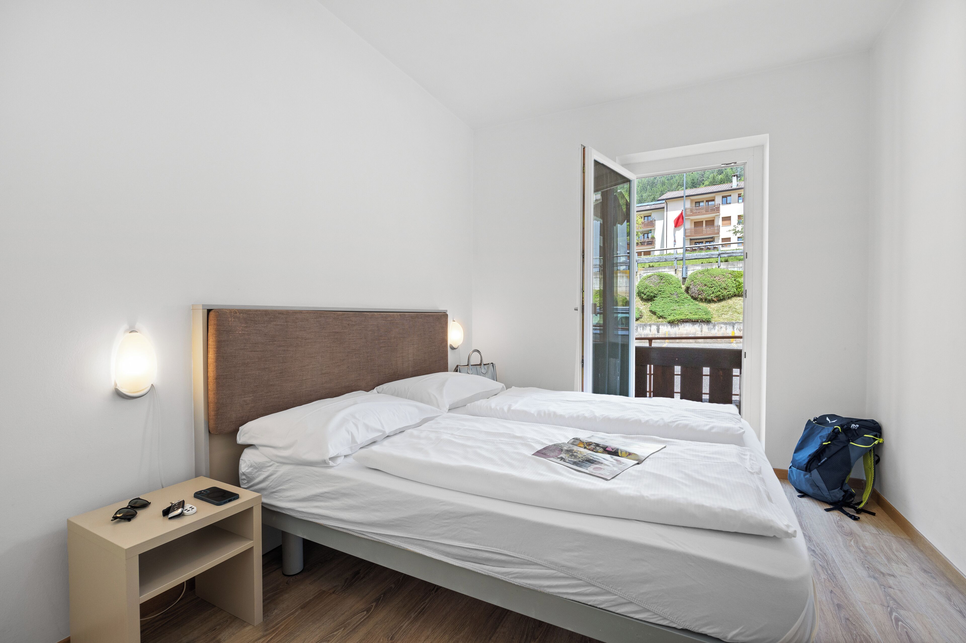 A modern hotel room with a bed, bedside table, and a view of the outside balcony.