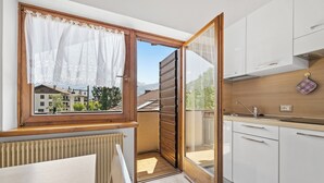 A compact kitchen with a view of the city, a wooden window frame, and a white cabinet. - Residence Lagorai (Tesero)