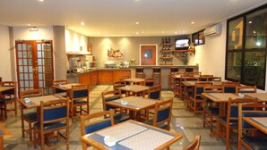 Un restaurante con varias mesas y sillas de madera, una zona de cocina y un televisor en la pared.